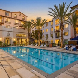 a pool in a courtyard with palm trees and lounge seating with umbrellas